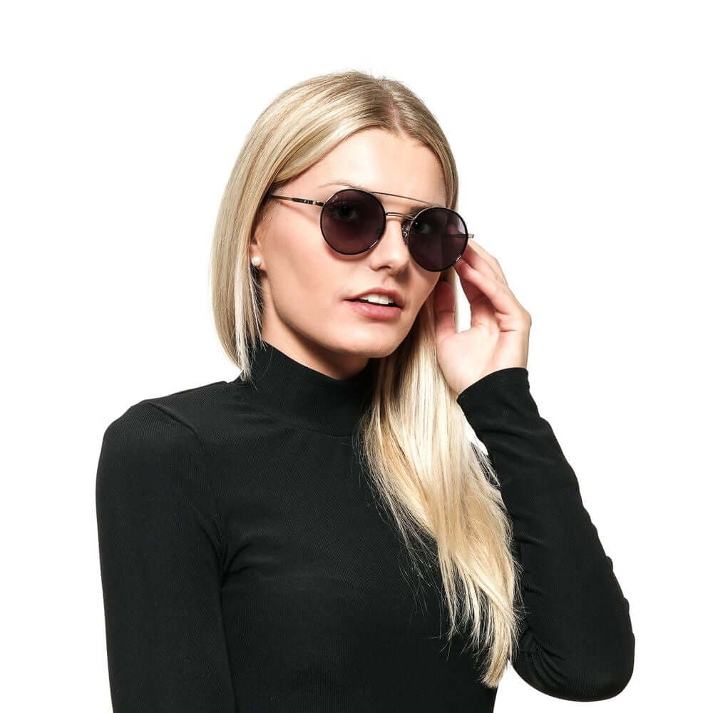 Woman wearing silver aviator sunglasses with grey lenses, black top, side view. Metal frame, full-rim style.