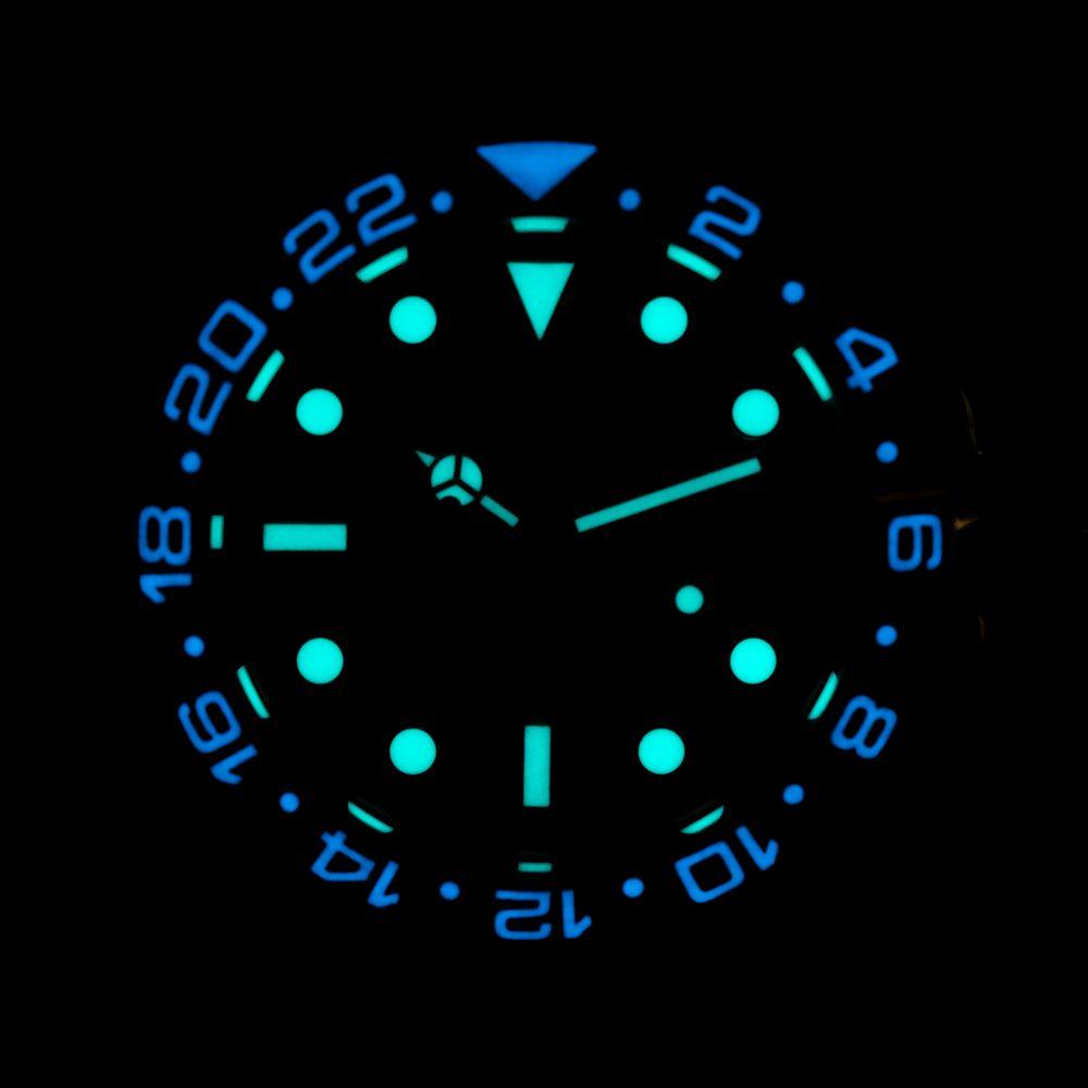 Glowing watch dial with luminous markers and hands, showing time against black background.