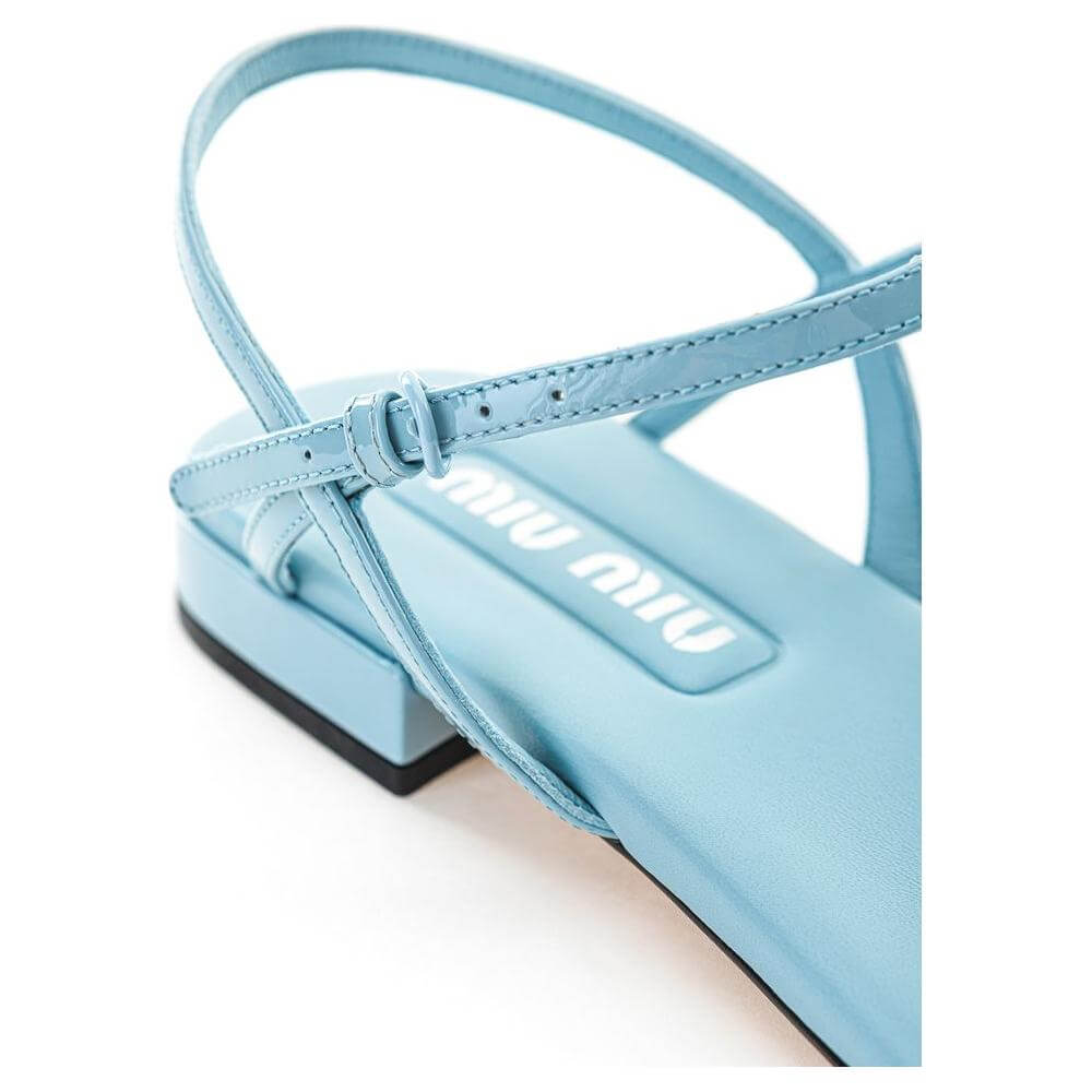 Close-up of Miu Miu blue patent leather sandal with logo lettering, thin straps, and black sole. Elegant and stylish design.