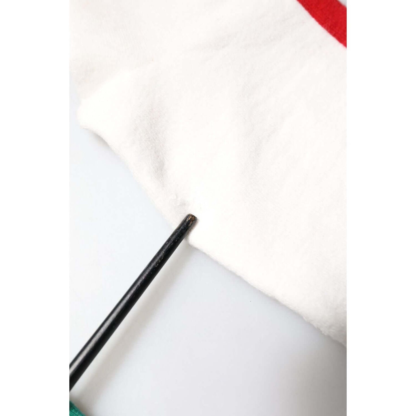 Close-up of a white Dolce & Gabbana cotton sock showing minor stain, highlighted with a pointer. Mid-calf length, multicolor design.