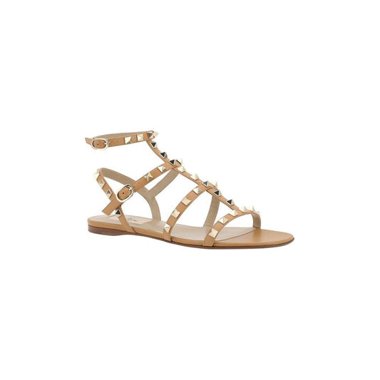 Valentino Garavani Rockstud leather sandals with ankle strap, flat sole, and iconic studs in nude color.