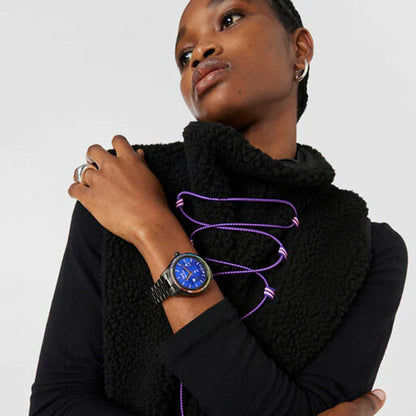 Person wearing TOUS WATCHES Mod. 200351040 with blue dial and black band, dressed in stylish black outfit with purple accents.