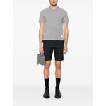 Man wearing Thom Browne T-shirts and Polos Light Grey with stripe detailing and logo patch, holding a case. Casual stylish look.